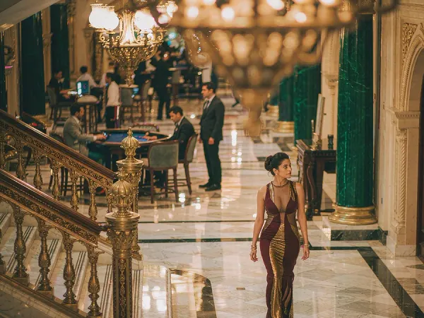 tr2026 Woman in a maroon and gold dress in a chandelier-lit casino lobby