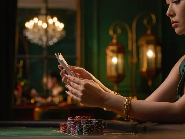 tr2026 Hands with gold bangles holding three cards above green felt beside chip stacks