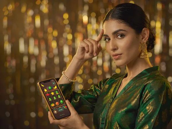 tr2026 Woman in an emerald and gold kameez holding a phone showing a glowing slot game